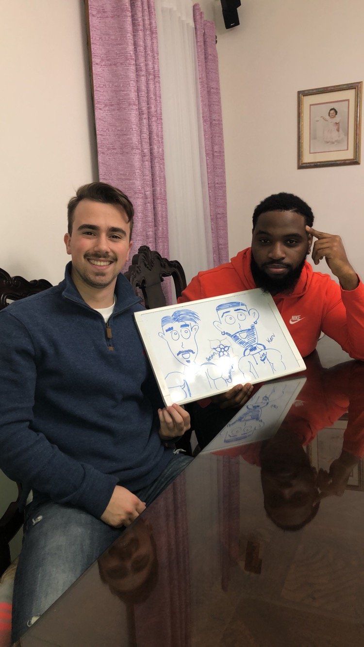 Two friends at a table holding up a whiteboard caricature they drew