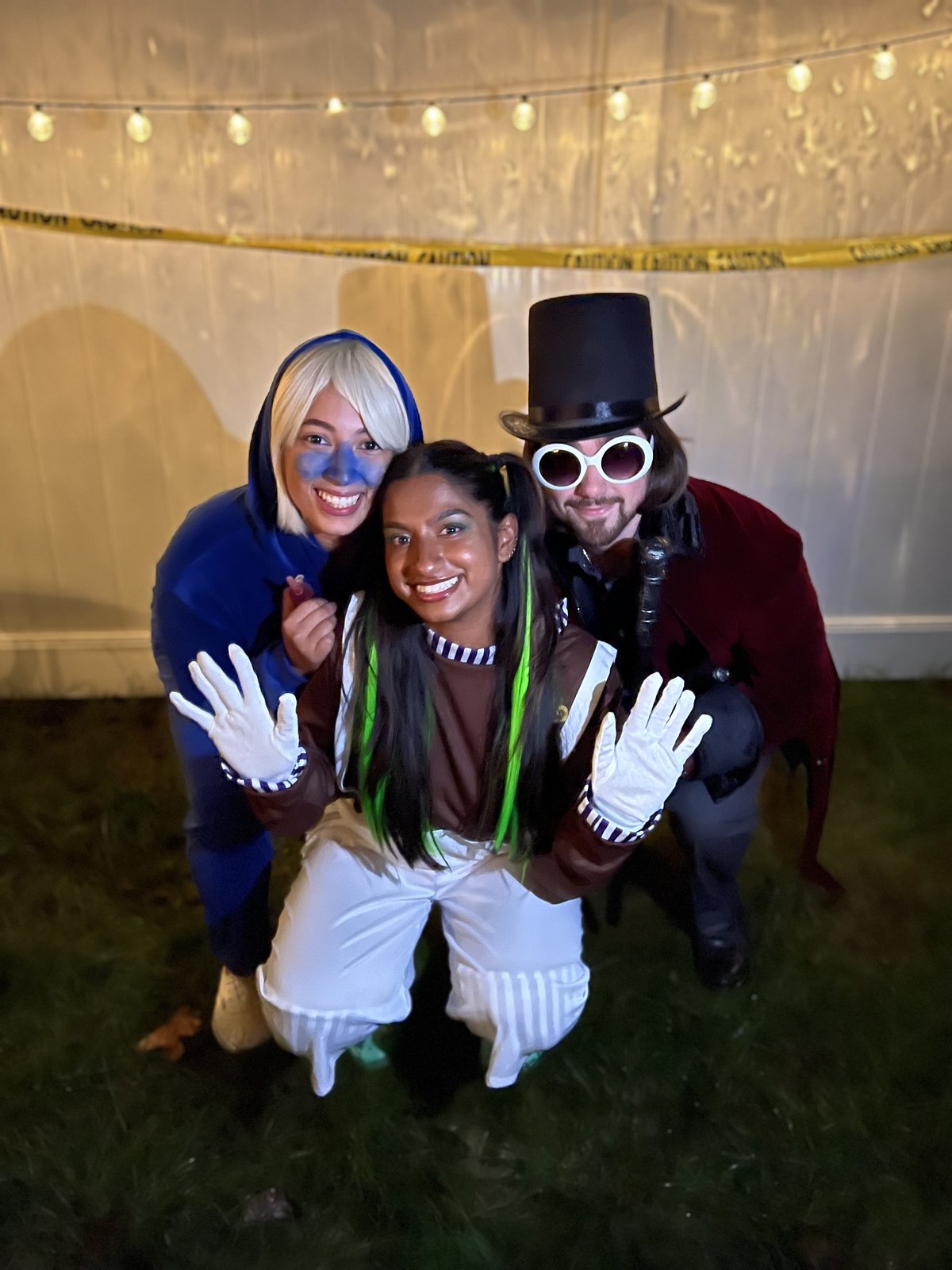 Three friends in costume outdoors under string lights