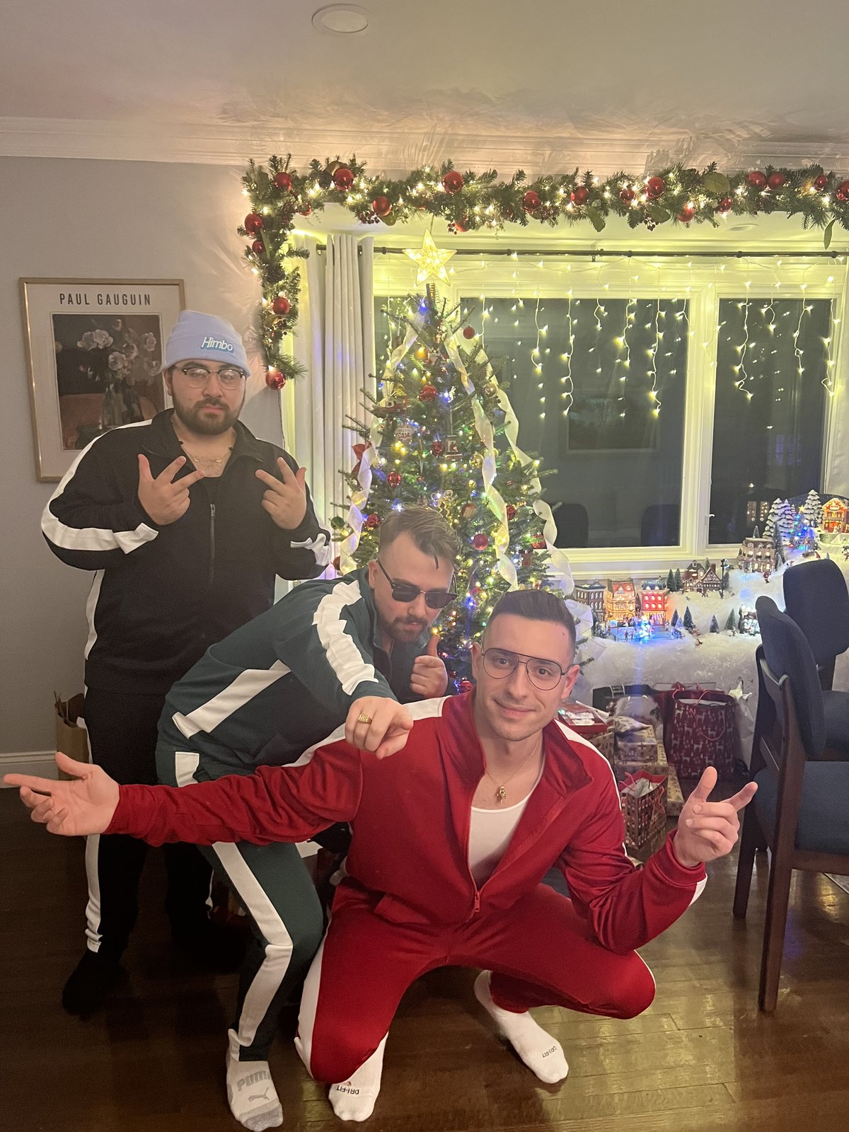 Three friends posing in tracksuits beside a decorated Christmas tree