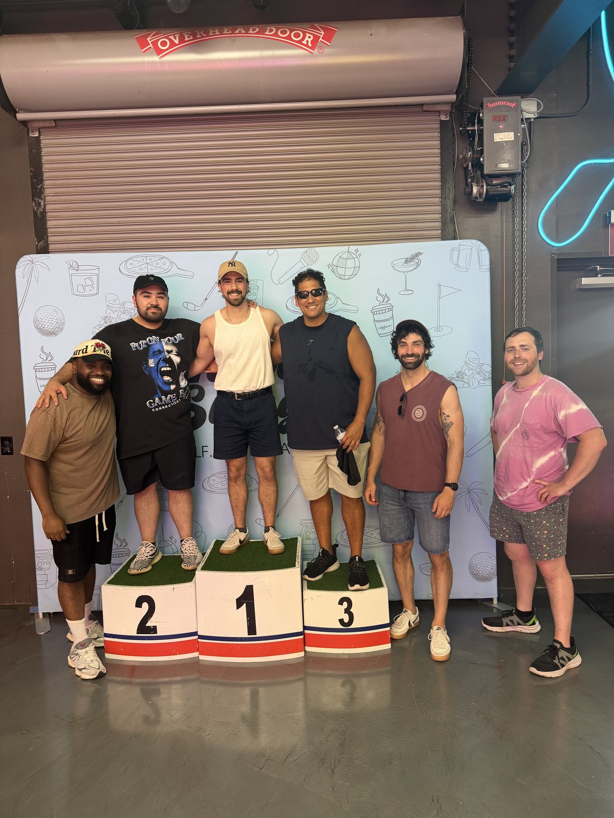 A group of friends gathered around a winners' podium at an arcade
