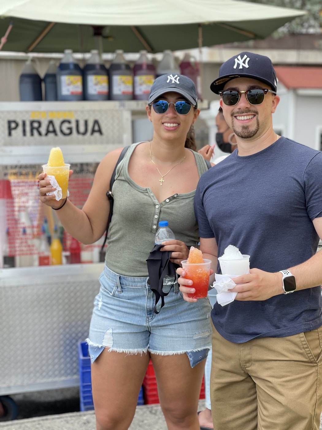 Austin and Bianca in baseball caps holding shaved ice at a piragua cart